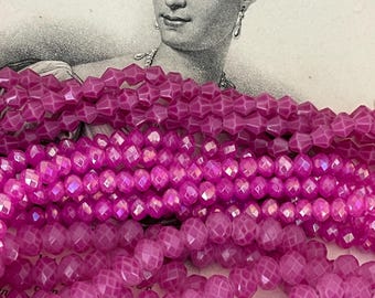 May include: A close-up of a strand of pink faceted glass beads. The beads are round and have a starburst pattern. The beads are arranged in a pile on a white surface with text in the background.