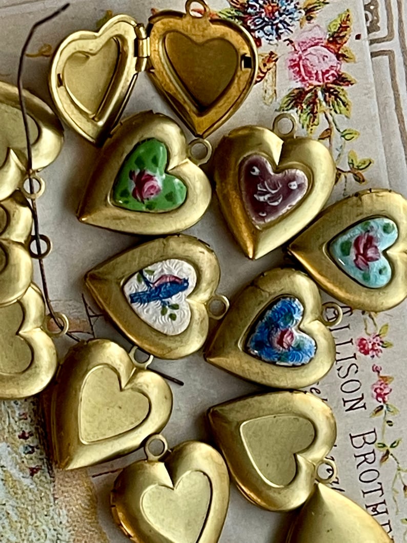 May include: A collection of gold heart-shaped locket pendants with various painted designs, including floral patterns, birds, and abstract designs.