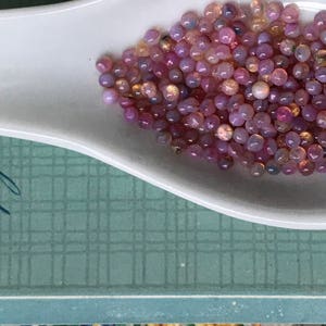 K&ouml;nnte beinhalten: Ein wei&szlig;er Keramikl&ouml;ffel gef&uuml;llt mit irisierenden rosa und wei&szlig;en Glasperlen.
