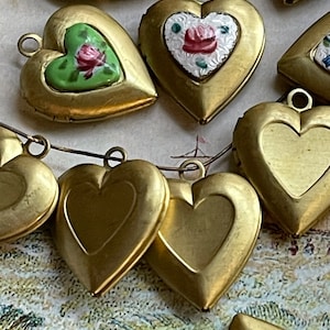 May include: A collection of gold heart-shaped locket pendants with various painted designs. Some lockets have floral patterns, while others are plain. The lockets are strung together with a thin chain.