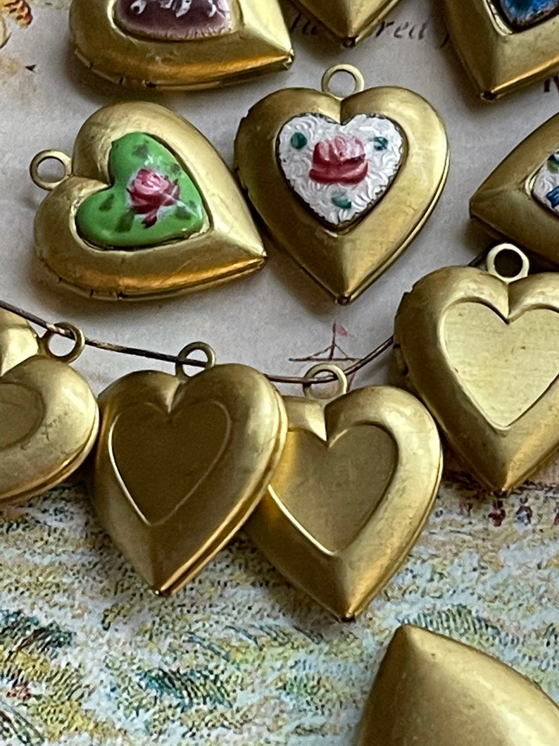 May include: A collection of gold heart-shaped locket pendants with various painted designs. Some lockets have floral patterns, while others are plain. The lockets are strung together with a thin chain.