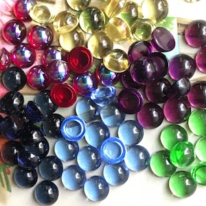 May include: Assortment of round glass cabochons in various colors, including red, purple, blue, green, and yellow. The cabochons are smooth and shiny, with a slight iridescent effect.