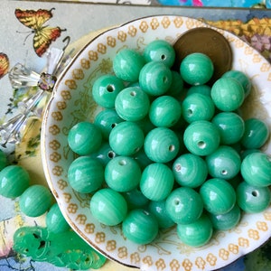 May include: A bowl of green jade beads. The beads are round and have a smooth, polished finish. They are arranged in a random pattern in the bowl.