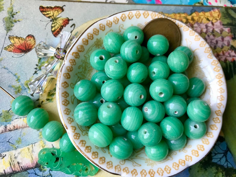 May include: A bowl of green jade beads. The beads are round and have a smooth, polished finish. They are arranged in a random pattern in the bowl.