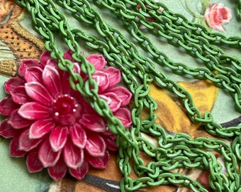 May include: A green chain necklace with a pink flower charm. The chain is made of metal and has a matte finish. The flower charm is made of plastic and has a glossy finish.
