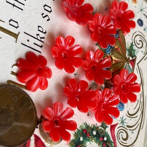 May include: Nine red plastic flower-shaped buttons with a hole in the center. The buttons are on a white background with a Christmas-themed design.