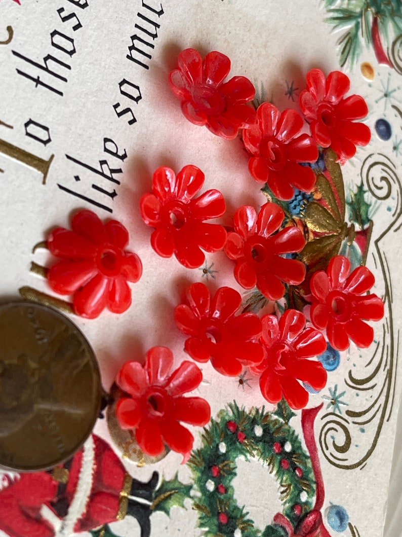 May include: Nine red plastic flower-shaped buttons with a hole in the center. The buttons are on a white background with a Christmas-themed design.