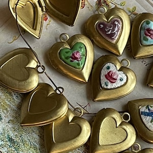 May include: A collection of brass heart-shaped locket pendants with various floral designs and a single locket with a bird design. The lockets are open and closed, revealing the interior of the lockets.