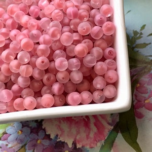 May include: A bowl filled with pink translucent round beads. The beads have a frosted finish and are perfect for jewelry making or crafting.