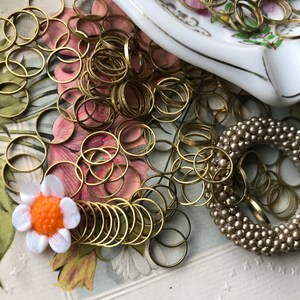 Peut inclure: Un grand tas d'anneaux de saut dor&eacute;s, une fleur blanche avec un centre orange et une bague en perles beige.