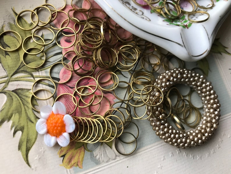 Peut inclure: Un grand tas d'anneaux de saut dor&eacute;s, une fleur blanche avec un centre orange et une bague en perles beige.