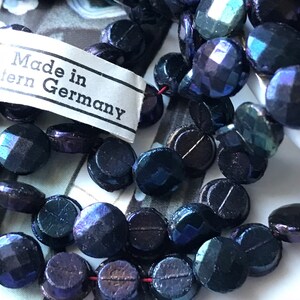 Puede incluir: Una hebra de cuentas de vidrio azul oscuro iridiscente con una etiqueta que dice "Made in Western Germany".