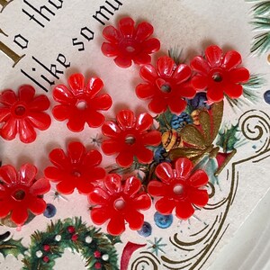 May include: A close-up of ten red plastic flower-shaped buttons. The buttons are arranged on a white card with a gold and green design. The card has the text "To those like so much" written on it.