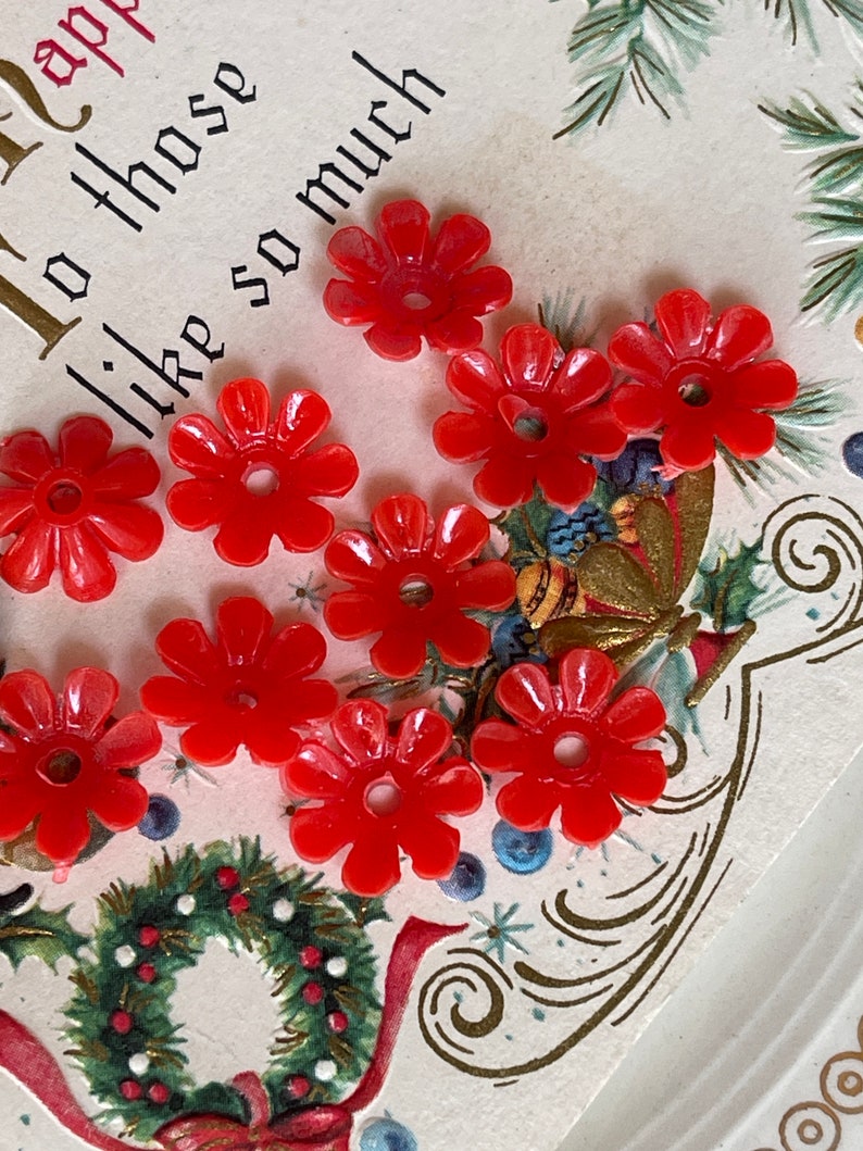 May include: A close-up of ten red plastic flower-shaped buttons. The buttons are arranged on a white card with a gold and green design. The card has the text "To those like so much" written on it.