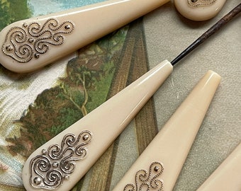 May include: Set of six ivory-colored sewing thimbles with gold filigree designs. The thimbles are shaped like teardrops and have a pointed end.