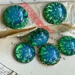 May include: Five round, iridescent green and blue glass cabochons with gold foil flecks.  Four of the cabochons are plain and one has a gold metal rim.
