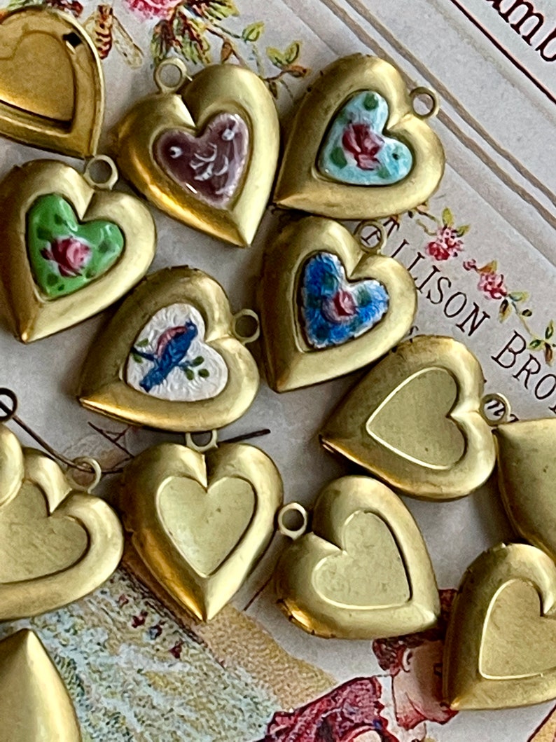 May include: A collection of gold heart-shaped locket pendants with various painted designs, including floral patterns, birds, and abstract designs.