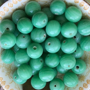 May include: A bowl filled with smooth, round, green jade beads. The beads have a light green color and a polished finish.