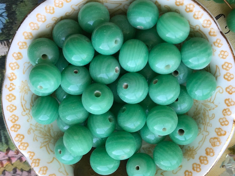 May include: A bowl filled with smooth, round, green jade beads. The beads have a light green color and a polished finish.