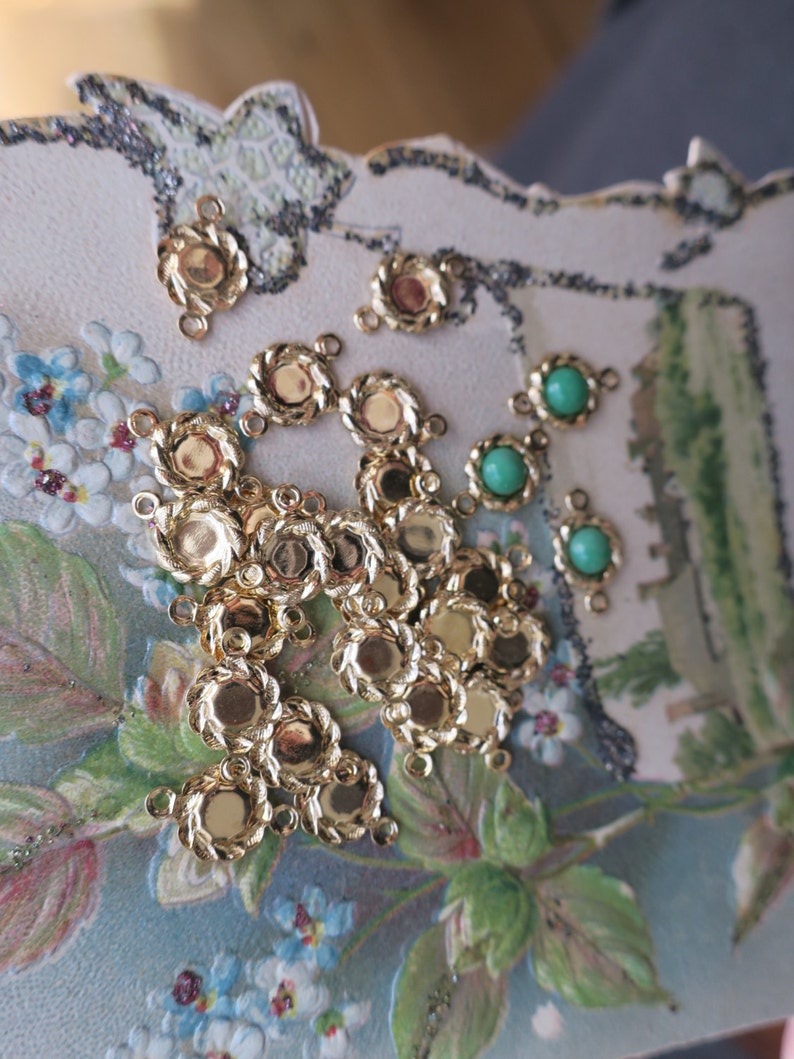 May include: A collection of gold-toned metal connector charms with a rope-like design and a round centre. There are also several green glass beads with a round shape.