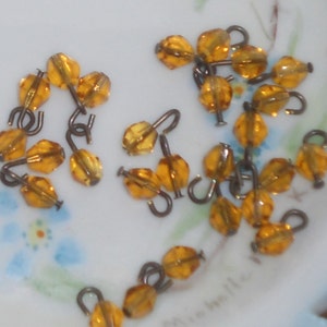 May include: A group of amber glass beads with metal hooks. The beads are faceted and have a shiny finish. The hooks are silver in color and have a simple design.