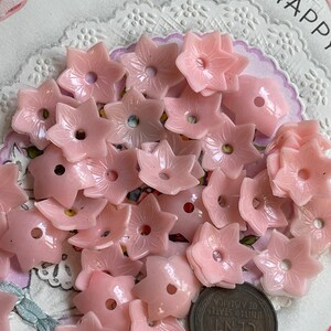 Peut inclure: Un ensemble de boutons en plastique rose en forme de fleur. Les boutons ont un trou au centre et sont dispos&eacute;s en pile.