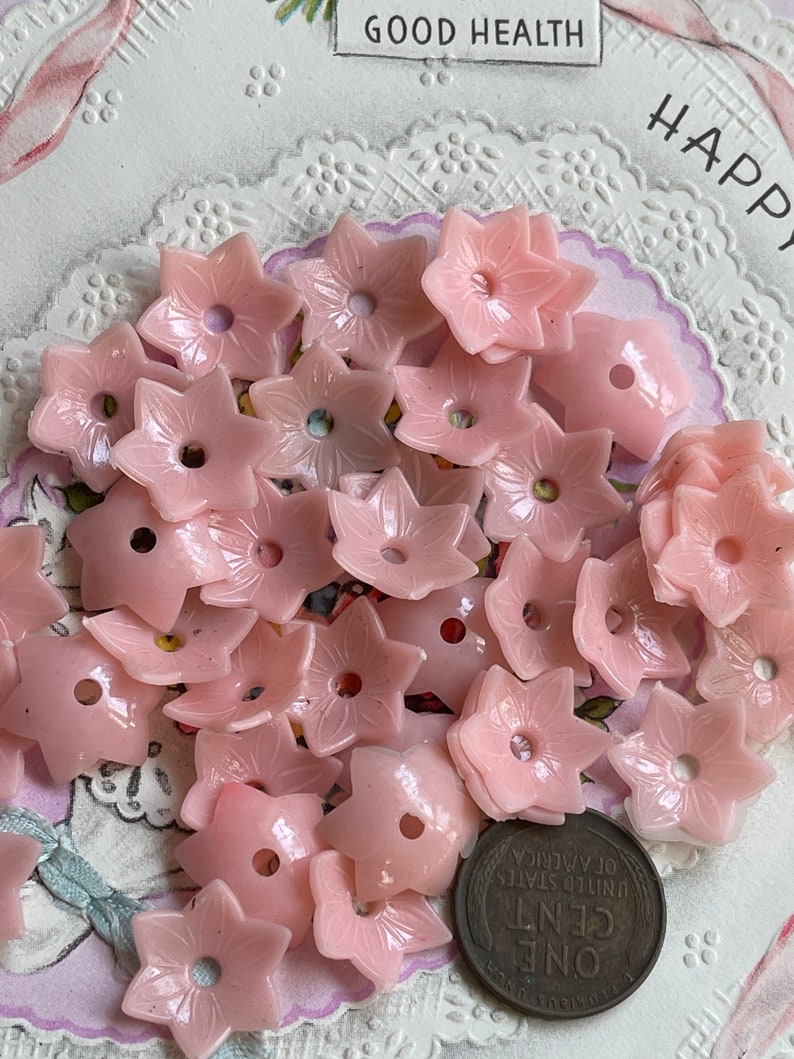 Peut inclure: Un ensemble de boutons en plastique rose en forme de fleur. Les boutons ont un trou au centre et sont dispos&eacute;s en pile.