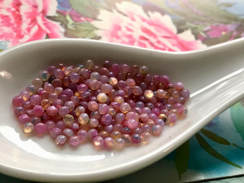K&ouml;nnte beinhalten: Ein wei&szlig;er Keramikl&ouml;ffel gef&uuml;llt mit schillernden rosa und wei&szlig;en Perlen. Die Perlen sind klein und rund und haben eine perlmuttartige Oberfl&auml;che.