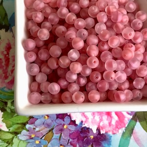 May include: A bowl filled with pink frosted glass beads. The beads are round and have a matte finish.