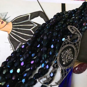 May include: A multi-strand necklace made of dark blue iridescent glass beads with a silver filigree clasp. The clasp features a black enamel oval with a silver floral design.