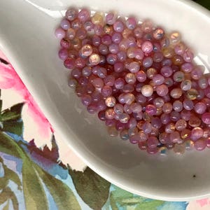 K&ouml;nnte beinhalten: Nahaufnahme einer wei&szlig;en Keramikschale, gef&uuml;llt mit einer gro&szlig;en Menge kleiner, runder, irisierender rosa und wei&szlig;er Perlen.
