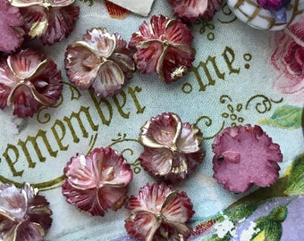 May include: A collection of pink and white flower-shaped buttons with gold accents. The buttons are arranged on a patterned surface with the word "Remember me." printed in gold lettering.