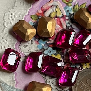 May include: Assortment of pink and gold faceted glass gems. The gems are in various shapes and sizes.