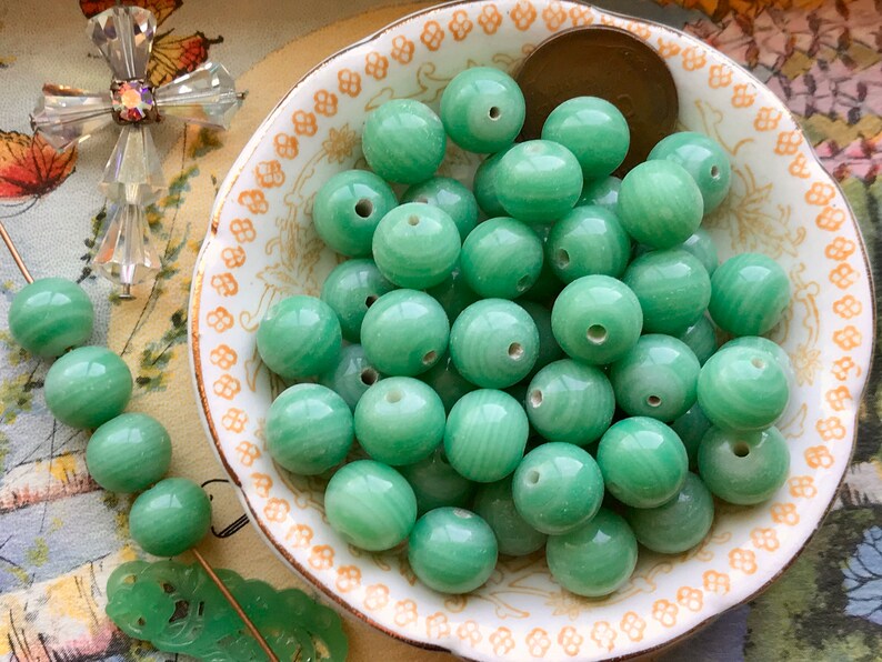 May include: A bowl of green jade beads. The beads are round and have a smooth, polished finish. They are perfect for making jewelry or other crafts.