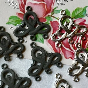 May include: A set of eight metal charms in the shape of a stylized knot. The charms are in two finishes: silver and black. The charms have three loops on each side for attaching to jewelry or other crafts.
