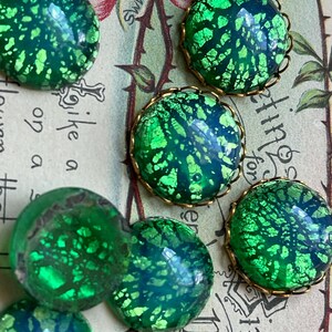 May include: A collection of round, green and blue iridescent glass cabochons with gold metal settings. The cabochons have a speckled, textured surface.