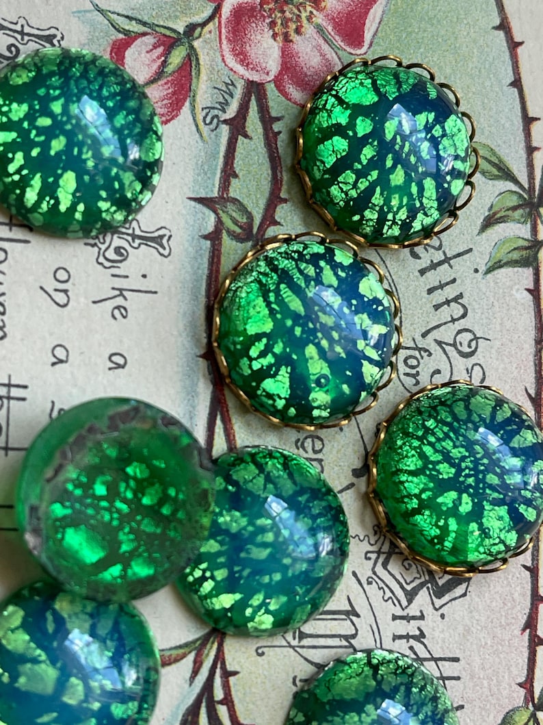 May include: A collection of round, green and blue iridescent glass cabochons with gold metal settings. The cabochons have a speckled, textured surface.