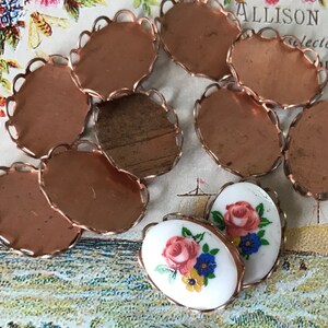 May include: Eight copper oval-shaped metal settings with scalloped edges. Two white porcelain cabochons with floral designs.