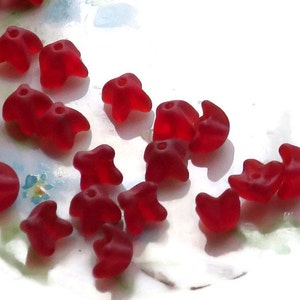 May include: A collection of red glass beads in the shape of stars and crescent moons. The beads are translucent and have a glossy finish.