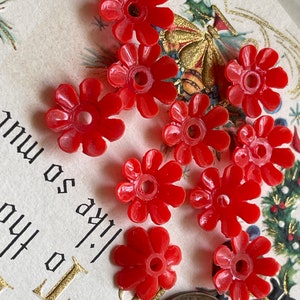 May include: Ten red plastic flower-shaped beads with a hole in the center. The beads are approximately 1 inch in diameter.