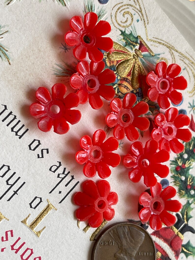 May include: Ten red plastic flower-shaped beads with a hole in the center. The beads are approximately 1 inch in diameter.