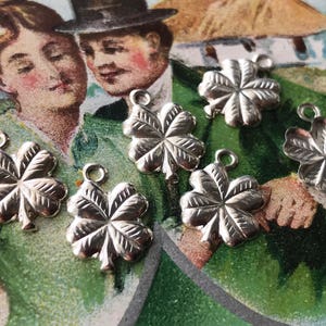 May include: Seven silver four-leaf clover charms with a textured finish. The charms have a loop at the top for attaching to a necklace or bracelet.