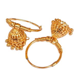 Può includere: Un paio di orecchini color oro con un design a forma di campana. Gli orecchini presentano intricati motivi a filigrana e piccoli accenti pendenti. La parte a cerchio degli orecchini è un design circolare semplice.