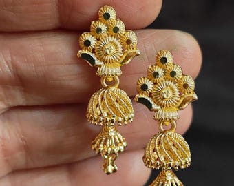 May include: A pair of gold-colored earrings. Each earring features a floral design at the top, with a bell-shaped pendant hanging below. The earrings have intricate detailing and a polished finish, reflecting light.