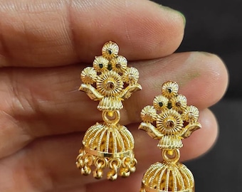 May include: A pair of gold-colored earrings. Each earring features a floral design at the top and a bell-shaped bottom with dangling accents. The earrings are held against a dark background.