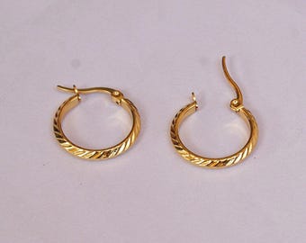 May include: A pair of gold-colored hoop earrings. Each earring has a textured, diagonal pattern around the hoop. The earrings are shown against a light background.