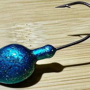 May include: A blue and green jig head fishing lure with a hook. The jig head is made of metal and has a textured finish.