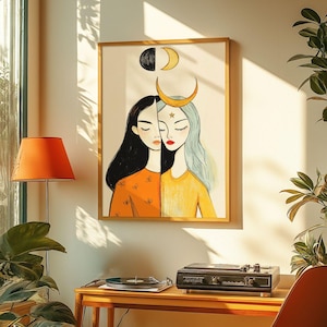 May include: A framed illustration of two women with long hair, one with black hair and the other with blue hair. They are both wearing yellow and orange clothing. The illustration is set against a white background with a crescent moon and stars.