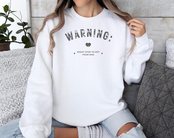 May include: White sweatshirt with the text "WARNING: MIGHT STOP TO PET YOUR DOG" in black with a small heart icon.