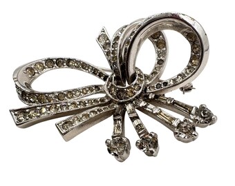 Broche vintage Kramer of New York em tom prateado com laço de fita e strass transparente.